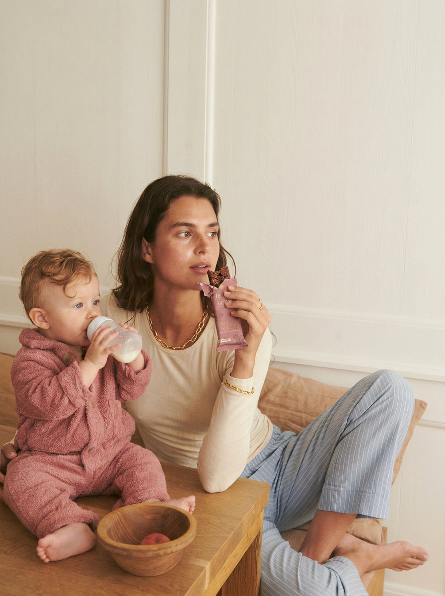 A mother enjoying a Berry Boost bar while her baby has a bottle